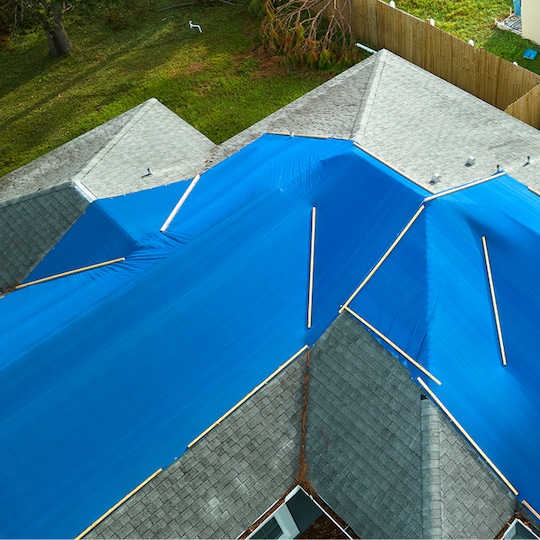A light green roof partially covered by blue tarps to protect it from storm damage.