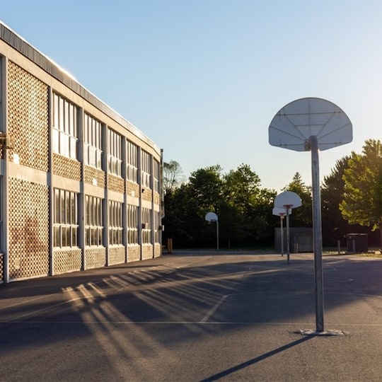 Schoolyard with basketball court and school building exterior in the sunny evening.