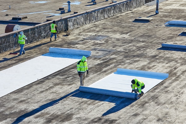 Contractors installing EverGuard® Fleece-Back single-ply membrane on a flat commercial rooftop.