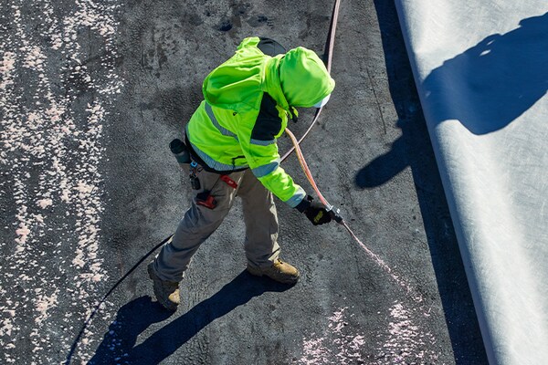 Contractor applying adhesive to flat rooftop.