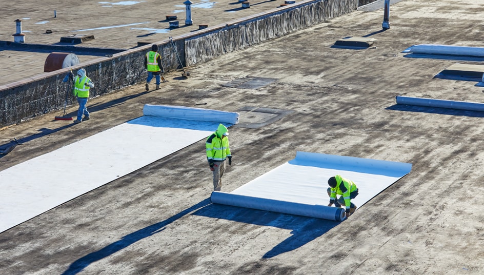 Contractors installing EverGuard® Fleece-Back single-ply membrane on a flat commercial rooftop.