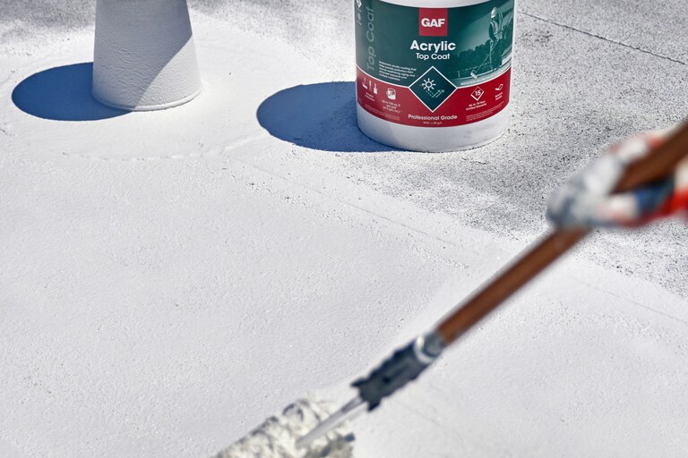 A contractor applying GAF Acrylic Coat Top Coat on a flat roof.