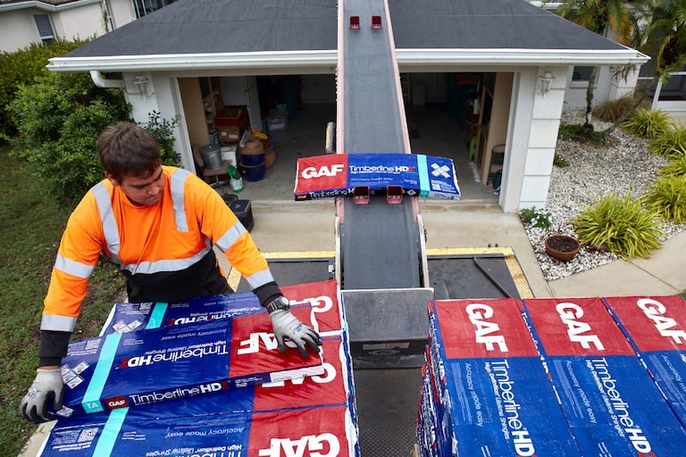 GAF contractor loading Timberline HDZ shingles onto conveyor belt to reach roof.