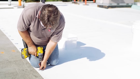 Up-close shot of contractor drilling plates into a seam for a mechanically attached system.